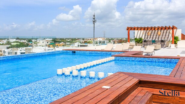 Piscina en la azotea con terraza de madera y sillones de descanso, rodeada de un paisaje urbano.