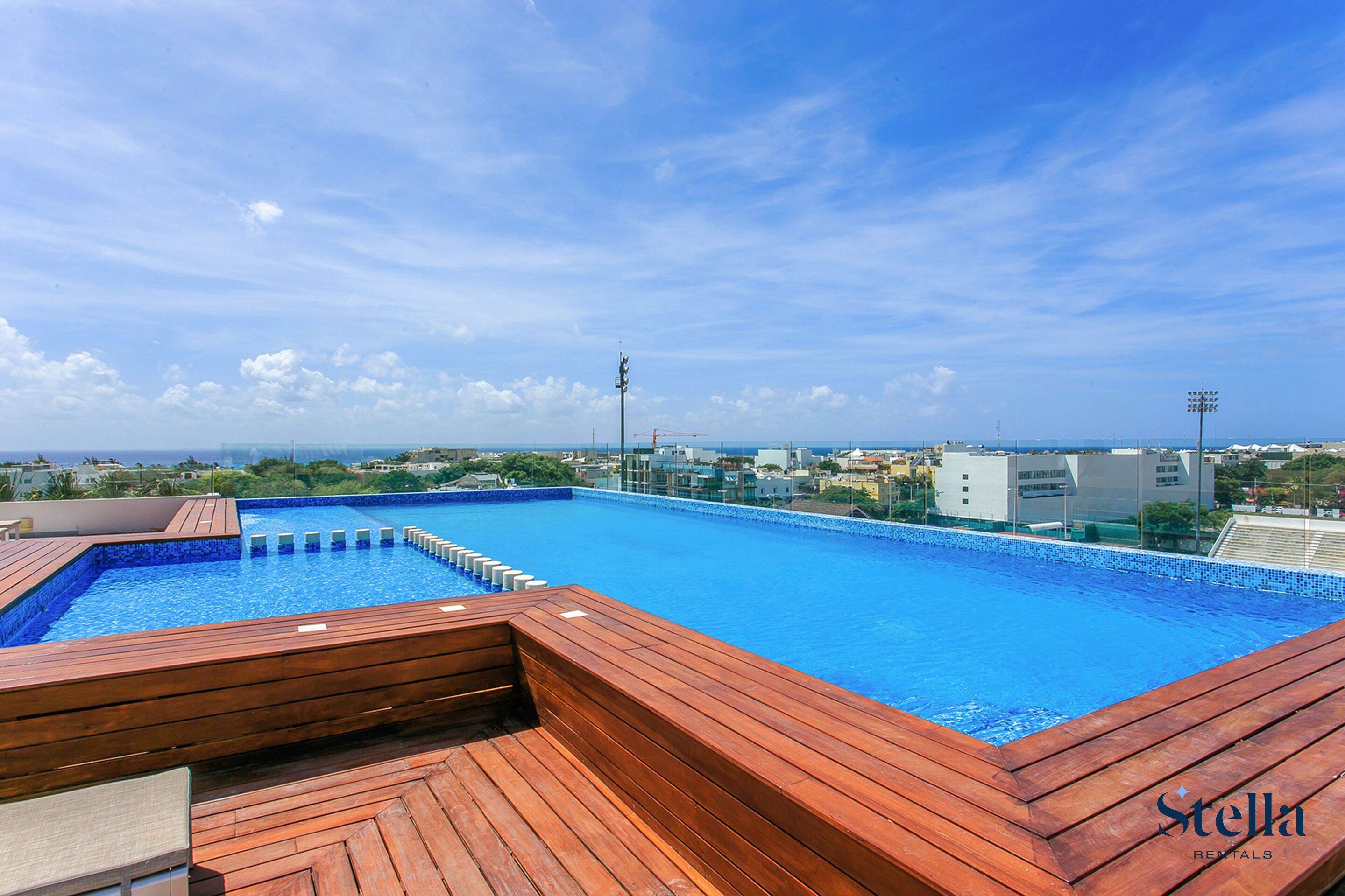 Piscina no terraço com deck de madeira e vista para a cidade.