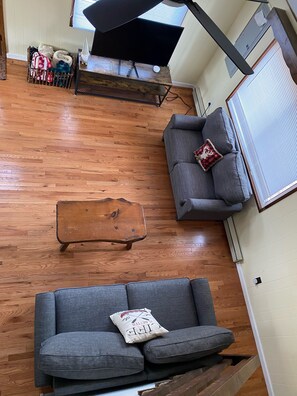 A living room with a wooden floor, a grey sofa, a wooden coffee table, and a TV on a stand.