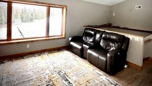 A room with a large window, a black leather sofa, a wooden bench, and a patterned rug. - Gracie- A spacious house near Swan Lake! (Pengilly)