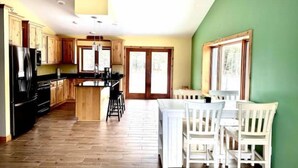 A modern kitchen with wooden cabinets, a black refrigerator, and a dining area with white chairs and a table. - Gracie- A spacious house near Swan Lake! (Pengilly)