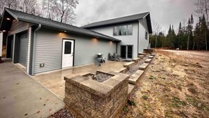 A modern two-story house with a covered patio area and a stone fire pit. - Gracie- A spacious house near Swan Lake! (Pengilly)