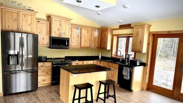 A modern kitchen with wooden cabinets, stainless steel appliances, and a central island with stools. - Gracie- A spacious house near Swan Lake! (Pengilly)