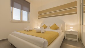 Habitació d'hotel moderna amb un llit gran, una taula de nit amb una làmpada i una finestra amb persianes.