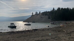 Ein Strand mit Booten, sandigem Ufer und einem bewaldeten Hügel im Hintergrund.