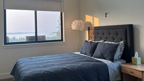 Ein Schlafzimmer mit einem Bett, einem Nachttisch, einem Deckenventilator, einem Fenster mit Blick und einer wandmontierten Leuchte.