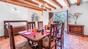 A dining area with a wooden table and chairs, a bench, and a view of greenery outside.