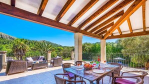 An outdoor patio with a wooden pergola, wicker furniture, and a table set for dining.