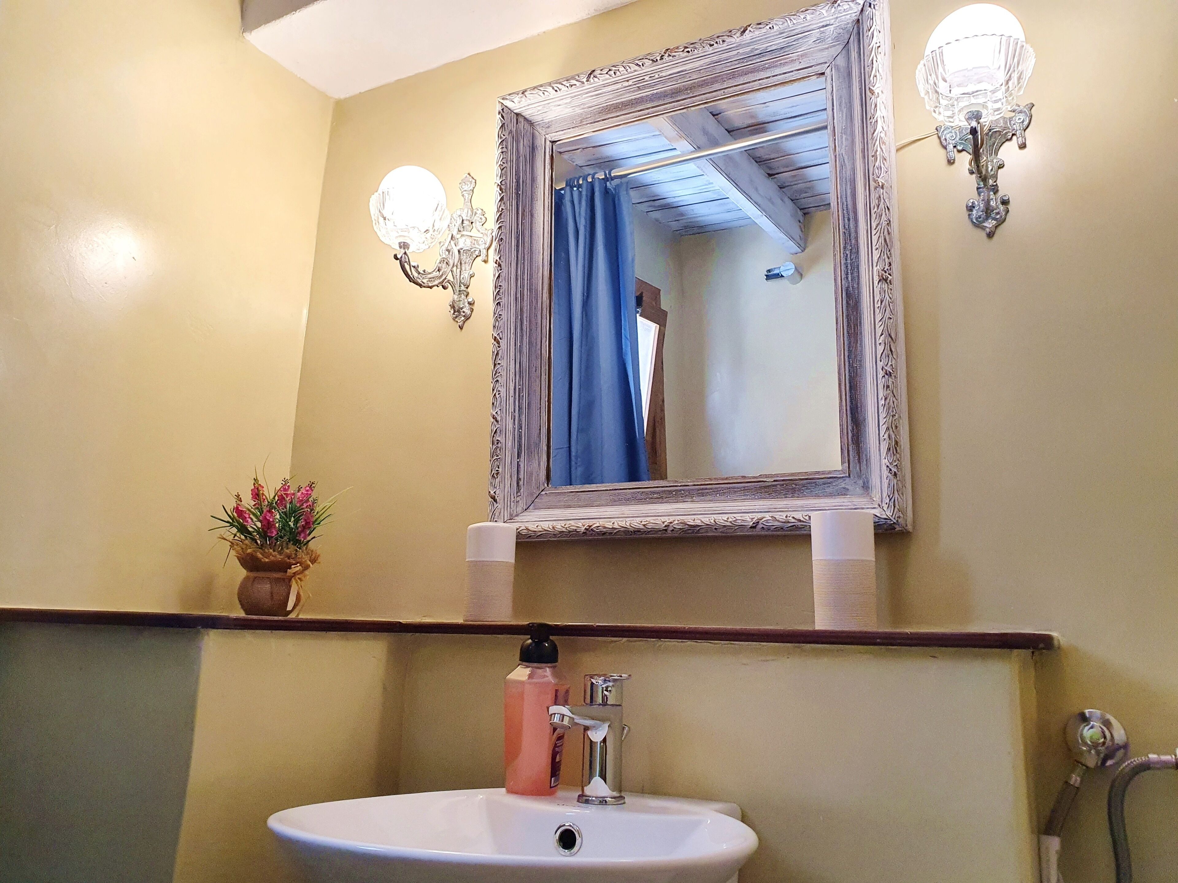 Une salle de bain avec un lavabo blanc, un miroir doté d’un cadre décoratif et deux appliques murales.