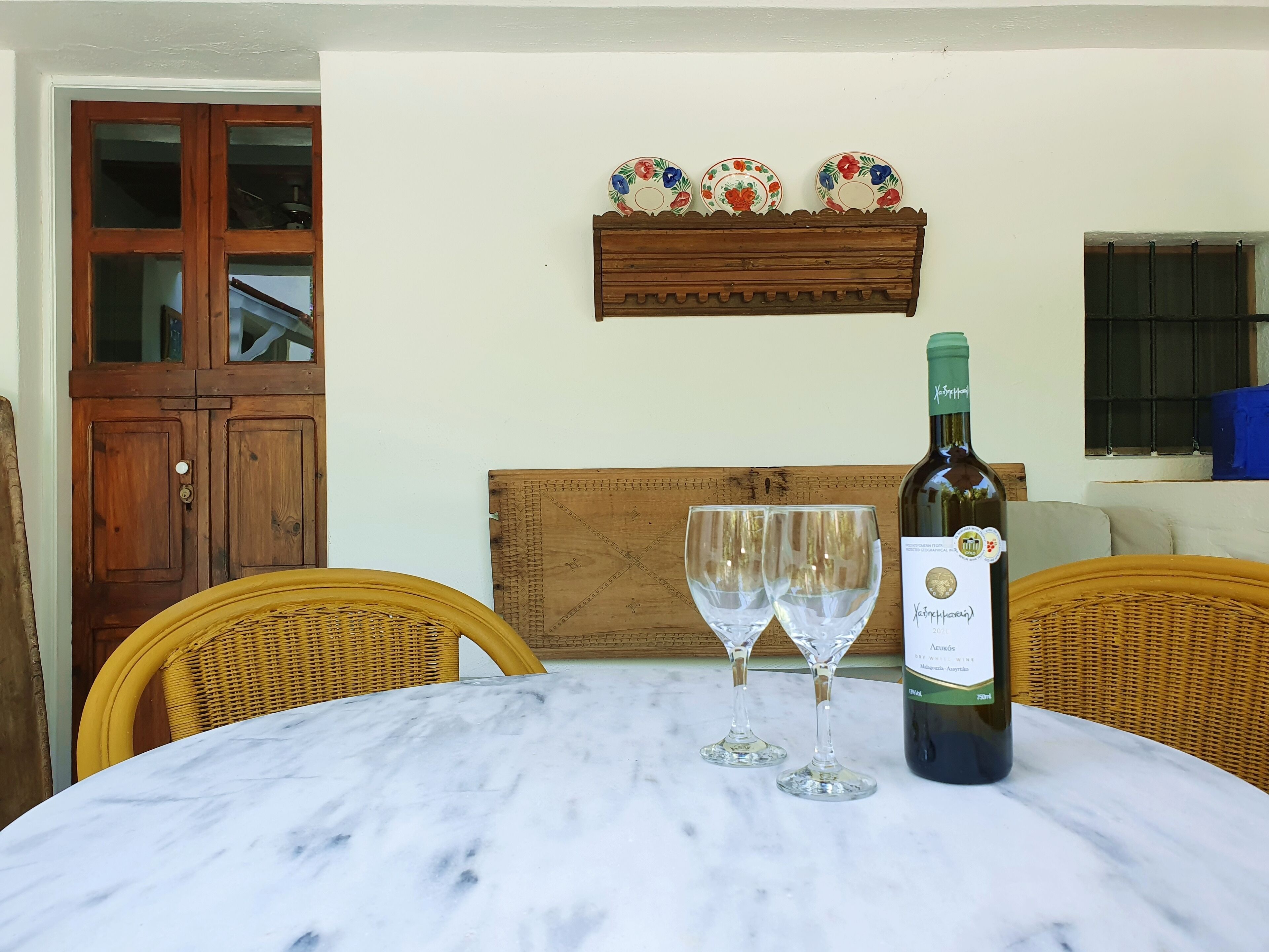 A marble table with two wine glasses and a bottle of wine, surrounded by wicker chairs.