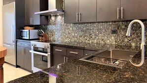 A modern kitchen with dark cabinetry, a stainless steel range hood, a microwave, and a granite countertop. - 3 bedroom 2 bath Ocean front condo on marina with opt boat slip.   (Key West)