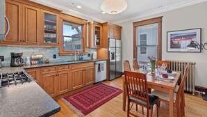 Une cuisine moderne avec des meubles en bois, un réfrigérateur en acier inoxydable et un coin repas avec une table dressée pour quatre personnes.