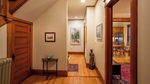 Un couloir doté d’un plancher en bois, une porte sur la gauche, une petite table avec un vase et une statue.