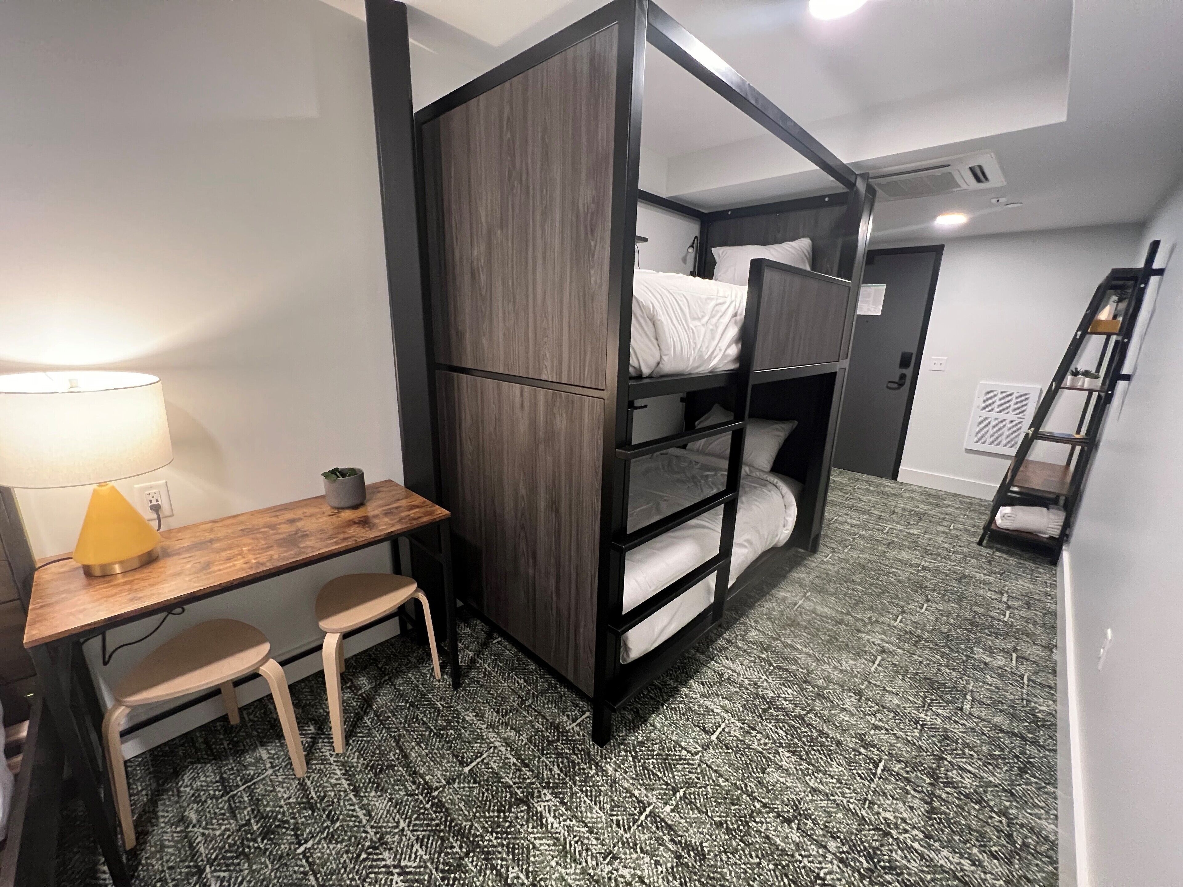 Dormitorio con literas, escritorio, silla, lámpara y escalera.