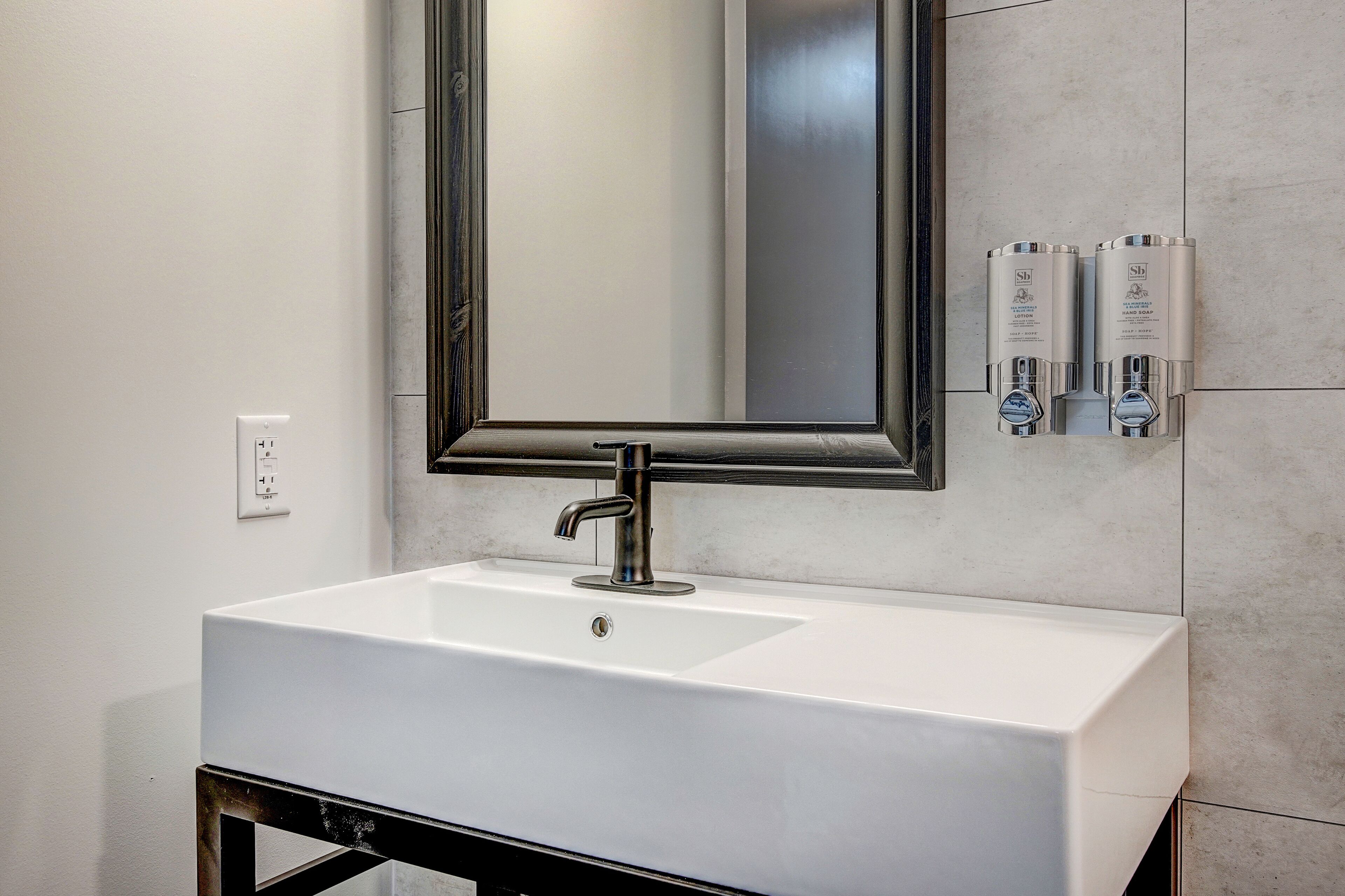 A bathroom with a white sink, a large mirror, and hand sanitizer dispensers on the wall.