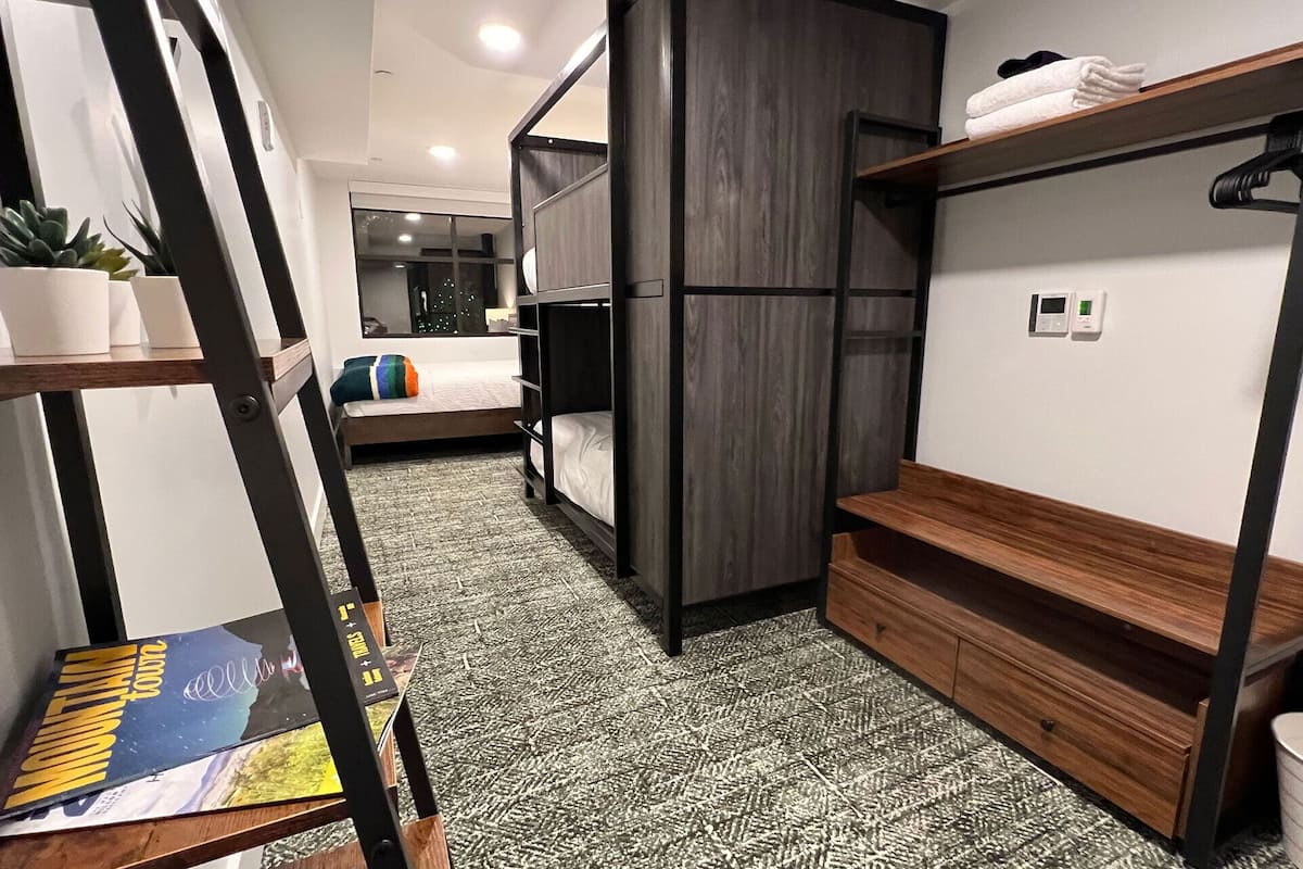 Habitación de hotel pequeña y funcional con literas, un escritorio y una estantería.