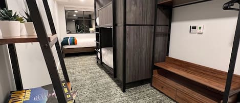 A compact hotel room with bunk beds, a small desk, and a bookshelf.