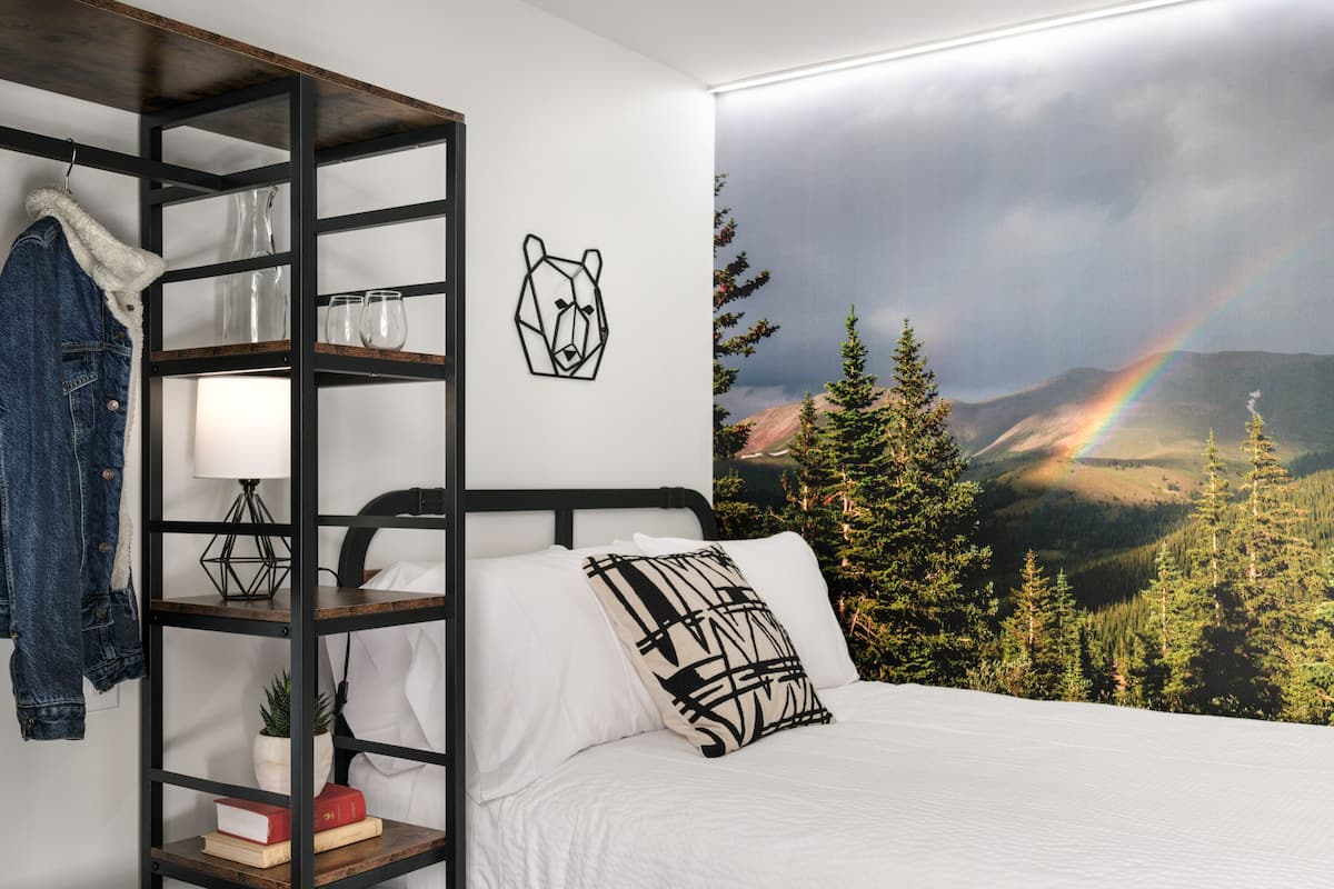 Un dormitorio con una cama, una estantería escalonada, una lámpara, una planta en maceta y un cuadro de un oso.