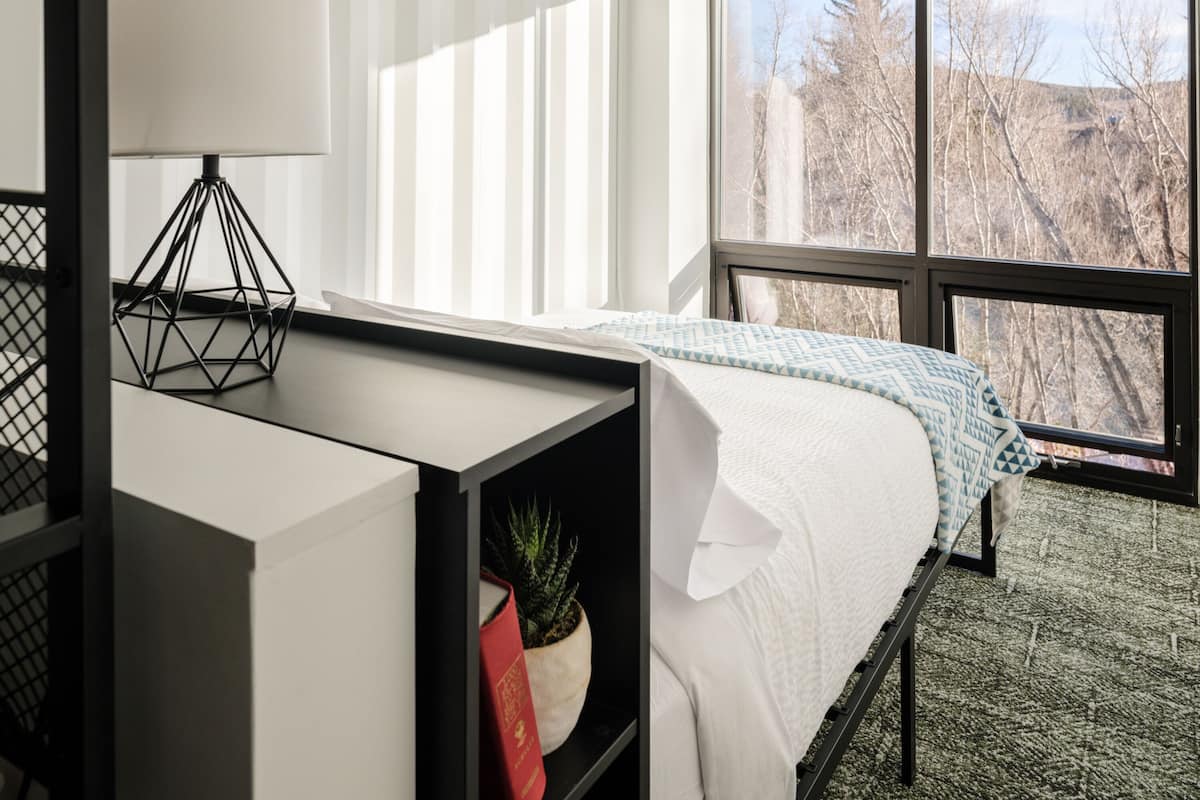 Un dormitorio moderno con cama, escritorio y ventana con vistas a árboles.