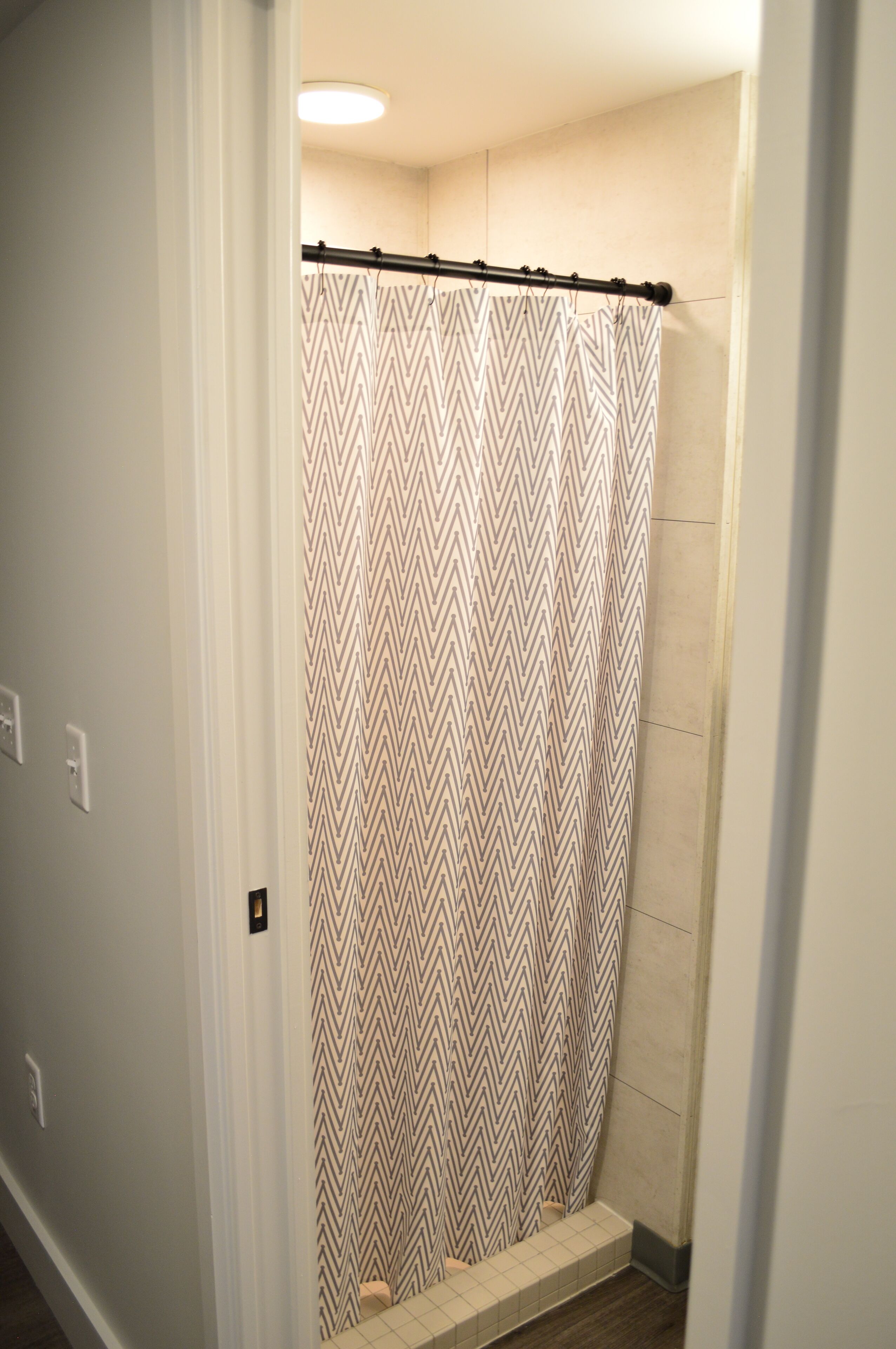 A bathroom with a shower curtain featuring a zigzag pattern, a tiled shower area, and a light fixture above the shower.