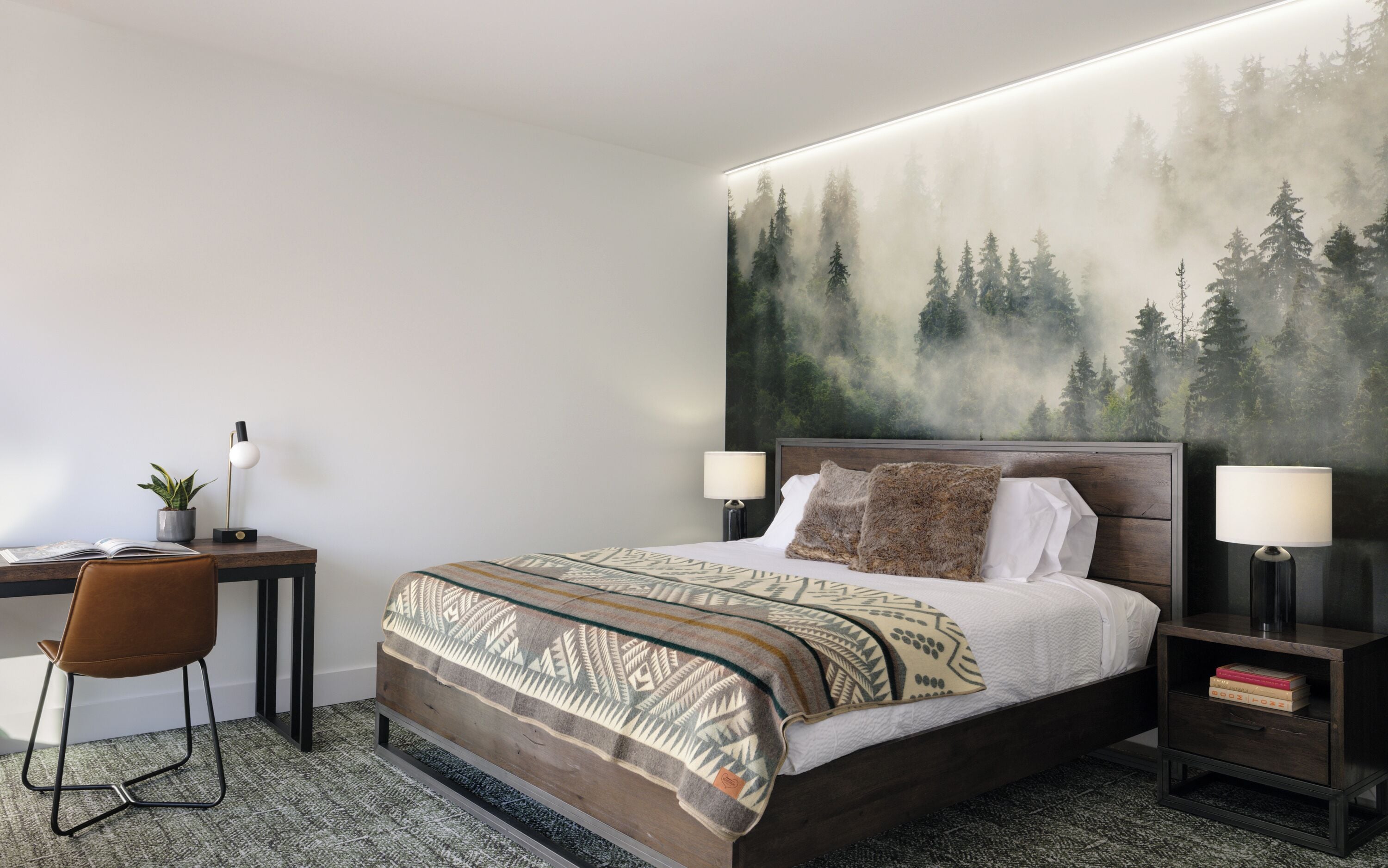 A modern hotel room with a large bed, a desk with a chair, and a nightstand with a lamp.