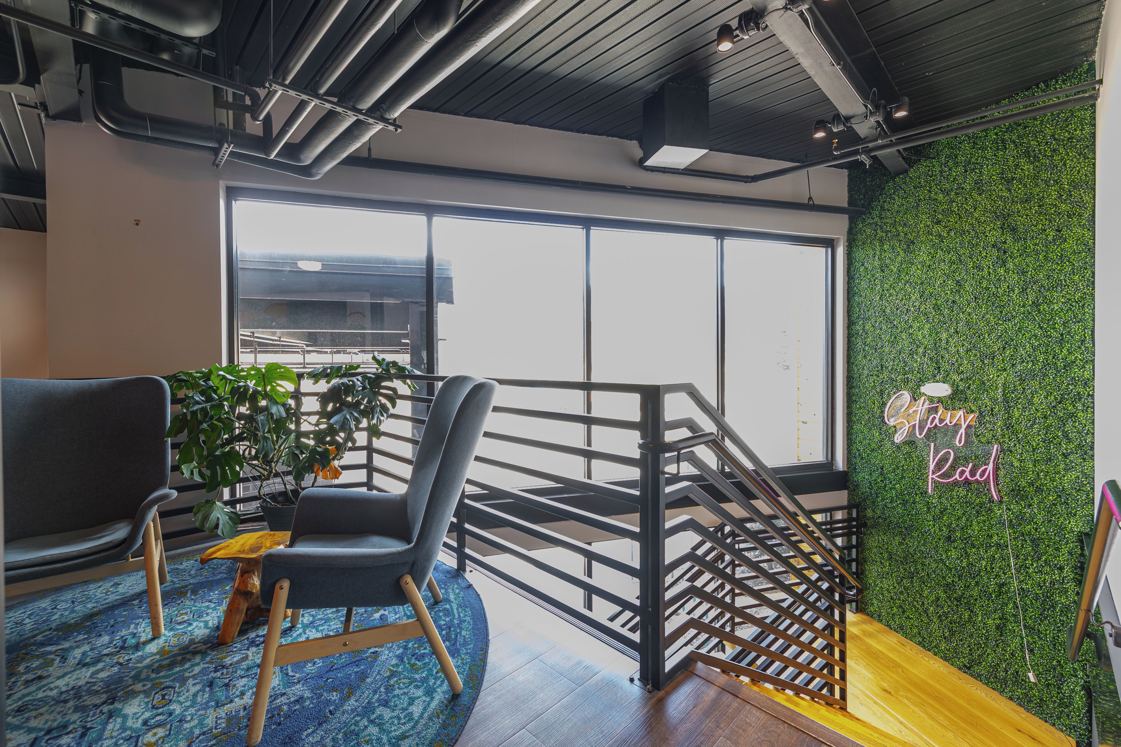 A modern interior with a staircase, a green wall with 'Stay Rad' signage, and a large window.