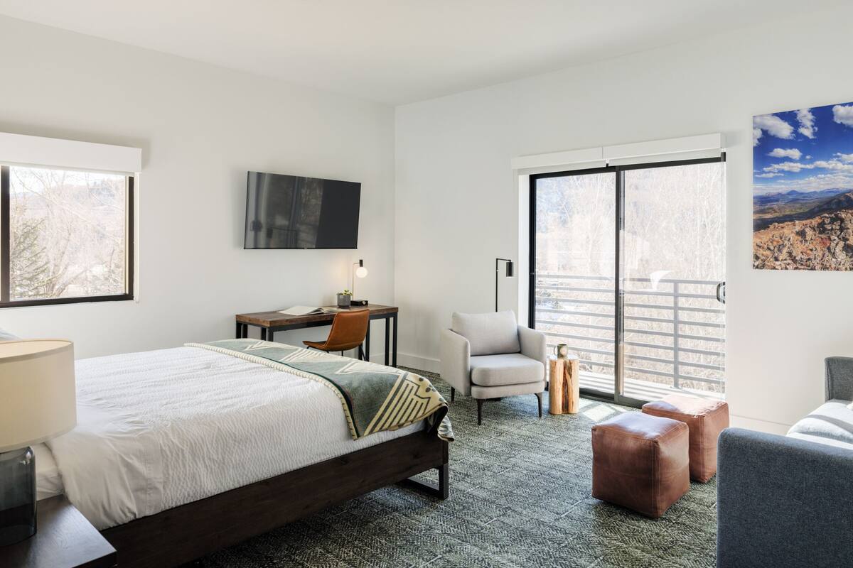 Habitación de hotel con cama, escritorio, sillón, sofá y una ventana grande con vista a la montaña.