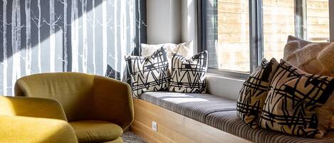 Een moderne kamer met een ingebouwde bank, een gele fauteuil en een groot raam met uitzicht op een houten gebouw.