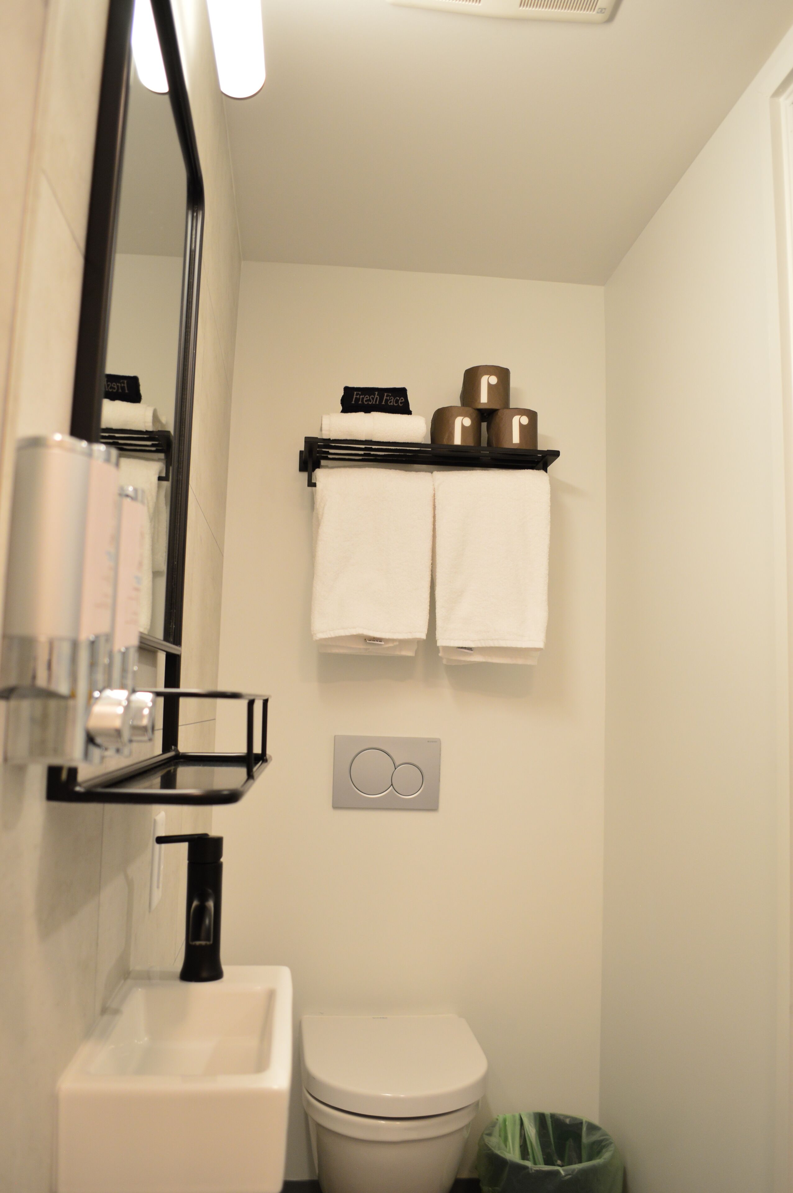 A bathroom with a white sink, toilet, and a mirror. There are two towels hanging on a shelf above the toilet.