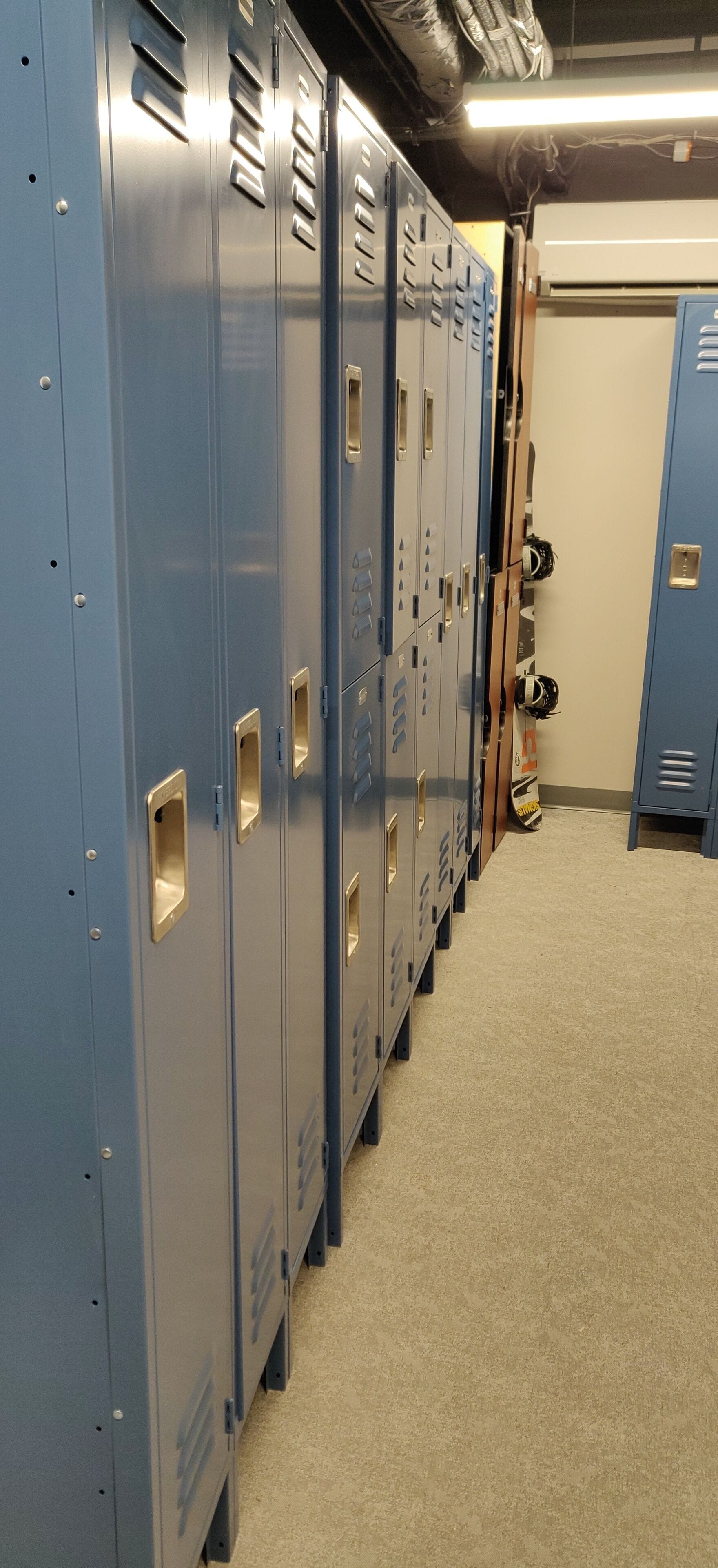 A row of blue lockers with a beige carpeted floor and a white door in the background.