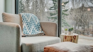 Un coin salon confortable avec un fauteuil rembourré, un coussin décoratif à motifs et une petite table d’appoint en bois agrémentée de plantes en pot.