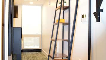 A hallway with a wooden floor, a metal ladder shelf, and a door with a frosted glass panel.