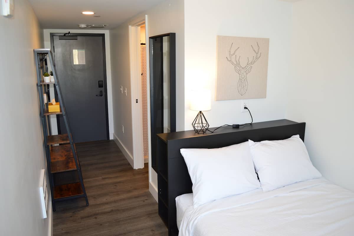 Un dormitorio con cama, escritorio, lámpara y una obra de arte en la pared.