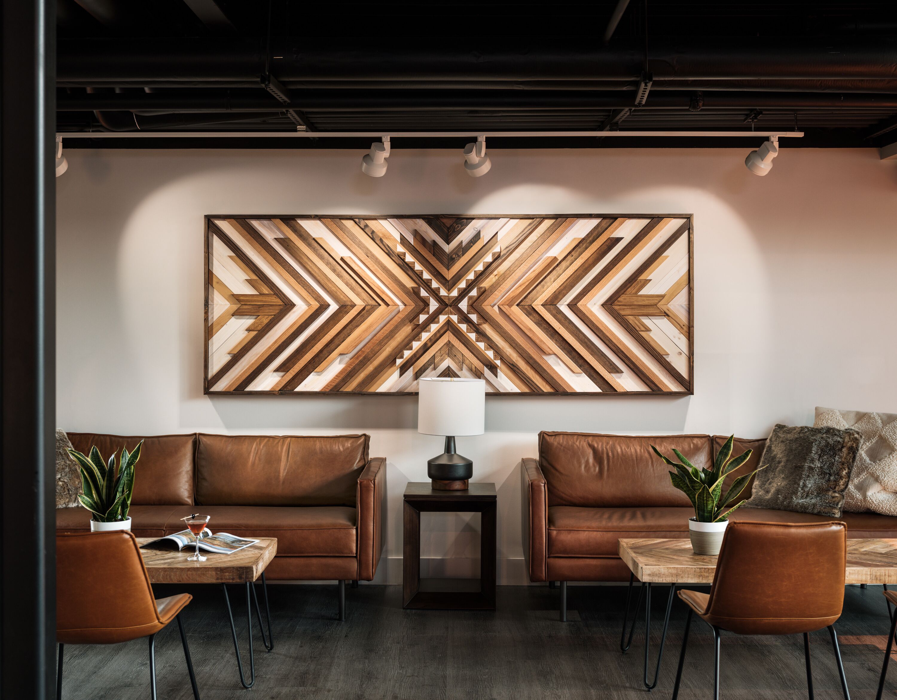 A modern lounge area with leather sofas, a wooden coffee table, and a large geometric wall art piece.