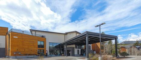 A modern building with a covered entrance, large windows, and a parking lot.