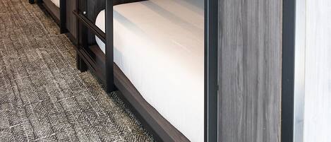 A row of bunk beds with wooden frames and white bedding, arranged in a hallway with patterned carpet.
