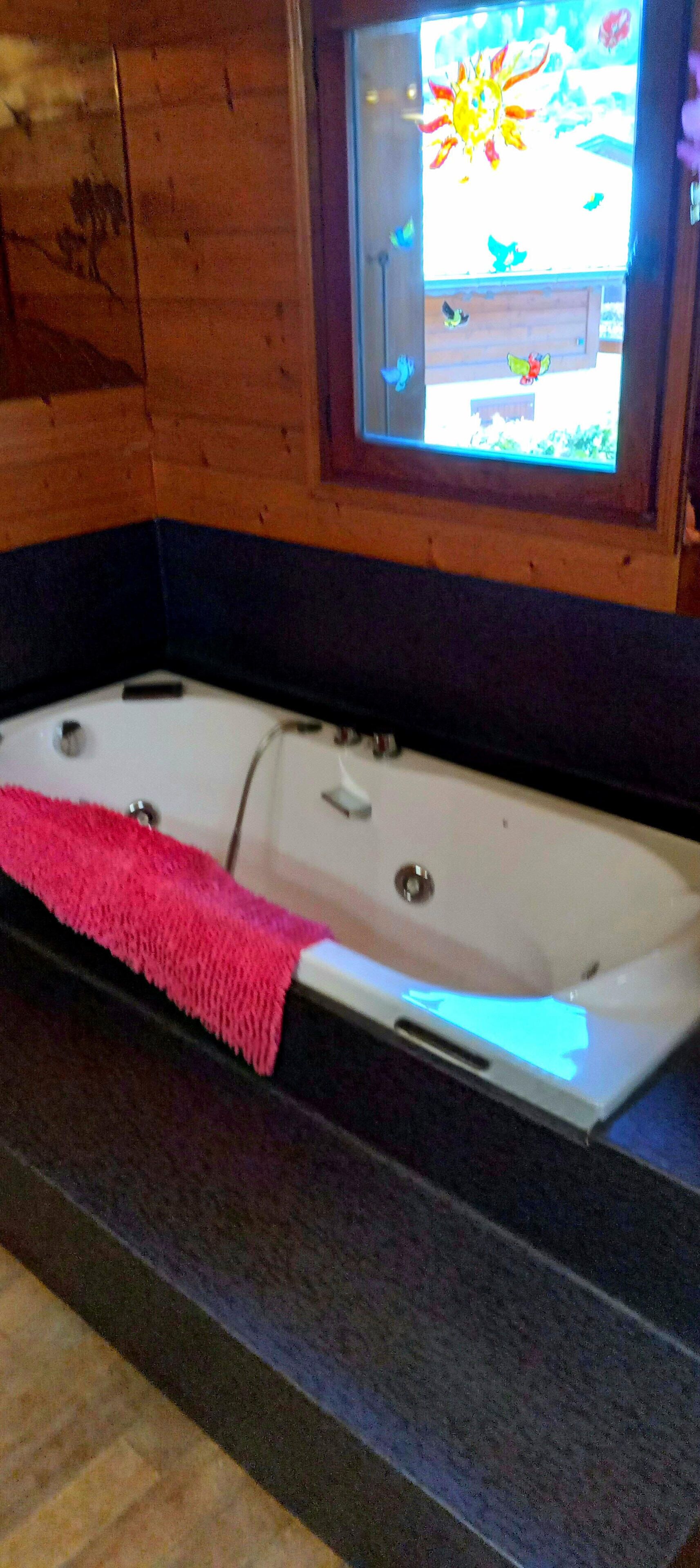 A bathroom with a large bathtub, a pink towel, and a window with a view of a garden.
