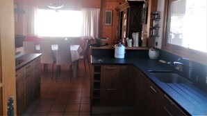 A kitchen with wooden cabinets, a sink, a stove, and a dining area with a table and chairs. - jlulbert's chalet near biotop lake and center (Combloux)