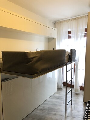 A compact kitchen with a built-in bench, a ladder, and a view of the outside through sheer curtains. - Studio (Sauze d'Oulx)