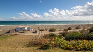 En fastighet vid stranden med en liten vit byggnad, en parkerad bil och ett inhägnat område.