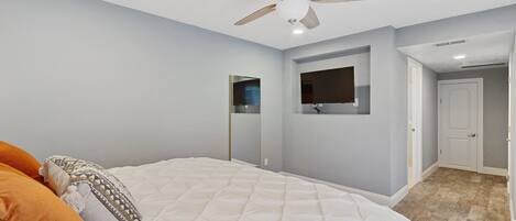 Een slaapkamer met een bed, een plafondventilator, inbouwverlichting, een deur en een gang.