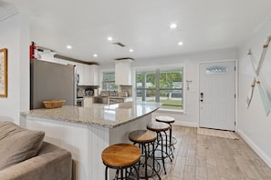 A modern kitchen with a central island, bar stools, and a view of the outdoors.