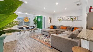 Un saló modern amb un sofà modular, una zona de menjador amb taula i cadires, i una cuina amb taulell i un extintor.