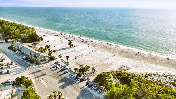 Luchtbeeld van een strand met een parkeerplaats, strandparasols en een uitkijktoren voor de strandwacht.