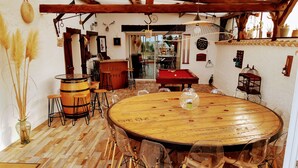 Taula de menjador de fusta envoltada de cadires, una taula de bitlles i una zona de bar amb tamborets.