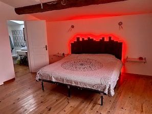 Quarto com cama, piso de madeira e luminária vermelha sobre a cama.