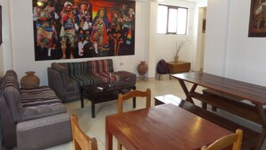 A living room with a sofa, a coffee table, a wooden dining table, and a large painting on the wall. - Pirwa B&B Cusco (Cusco)