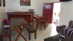 A dining area with a wooden table and chairs, a bar with a coffee machine, and a television mounted on the wall. - Pirwa B&B Cusco (Cusco)