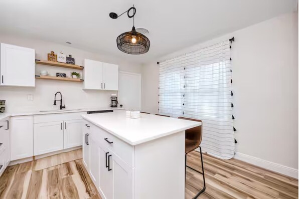 A modern kitchen with white cabinetry, a central island, and a hanging light fixture.