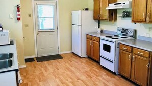 A compact kitchen with wooden cabinets, a refrigerator, an oven, and a microwave.